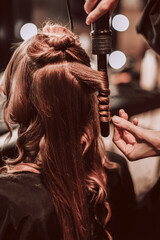 Fototapeta premium Female hands of a stylist doing a hairstyle of a young fashion model, back view