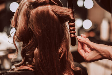 Naklejka premium Female hands of a stylist doing a hairstyle of a young fashion model, back view