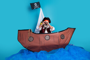 Photo of old pirate in traditional costume swimming searching ship isolated on blue color background