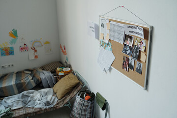 Noticeboard with photos of missing people and printed paper documents hanging on wall above sleepers of refugees