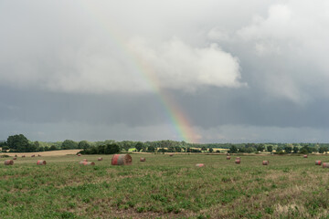 Rural landscape. Mown field and rolls of straw. Nature after the rain. Rainbow in the sky.