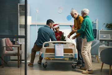Fototapeta premium Family decorating Christmas tree and making photo together with sick girl while she having treatment in hospital