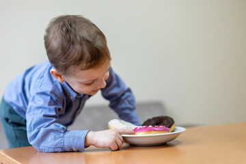 Curious boy reaching for a plate of donuts. A young boy in a blue shirt eagerly reaches for a plate...