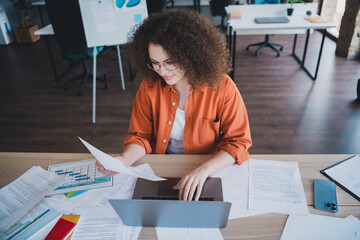 Young female professional reviewing documents at her desk in a modern office setting during...