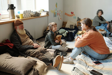 Happy cute child with toy looking at his mother during talk while both sitting on sleepers among...