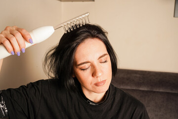 A woman uses a white handheld device on her head for a darsonvalization procedure. She has short black hair and a focused expression. The image emphasizes self-care and modern tools.