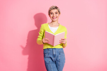 Young Woman Holding a Book Against Pink Backdrop Demonstrating Cheerful and Relaxed Style in Casual...