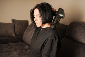 Using a percussion massager, the woman targets her leg muscles in a quiet living room. Her casual black outfit complements the serene environment. Perfect depiction of modern relaxation tools.
