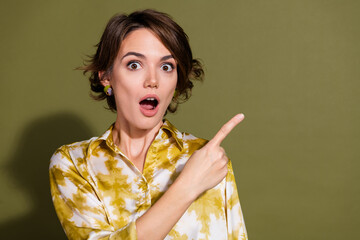 Surprised young businesswoman in elegant blouse against khaki background pointing at something...