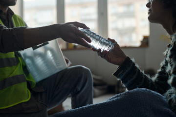 Hand of young female refugee and that of male volunteer passing bottle of water to settler of crisis camp for people in trouble