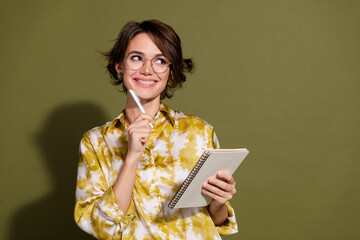 Confident young businesswoman with thoughtful expression, holding pen and notebook, wearing stylish...