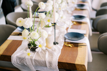 Bouquets of white flowers stand on a narrow fabric on a festive table with black plates