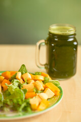 Fresh fruit salad with green smoothie on wooden table