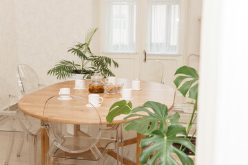 Cozy dining setting featuring a round wooden table surrounded by transparent chairs, complemented by lush green potted plants, creating a warm and inviting interior atmosphere.