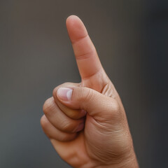 A close-up studio shot of a light-skinned human hand with the index finger pointing upwards against a plain gray background