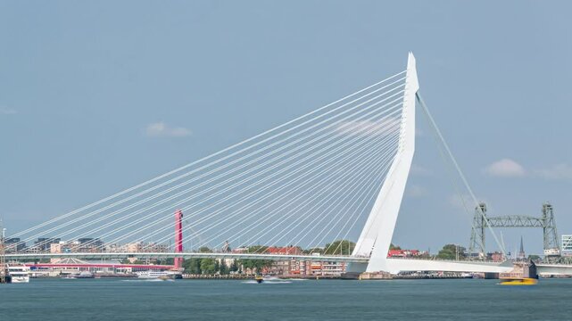 Erasmus Bridge timelapse, called The Swan, spanning the Maas River in Rotterdam, Netherlands. Holland's largest cable-stayed bascule bridge with waterfront, boats and a cloudy blue sky backdrop
