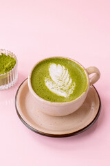 Matcha latte in a beige cup near a jar of matcha powder isolated on the pink background 