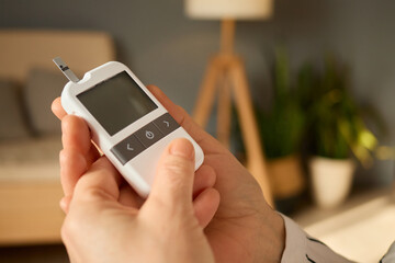 A person is holding a glucometer in a comfortable room, preparing to check their blood sugar...