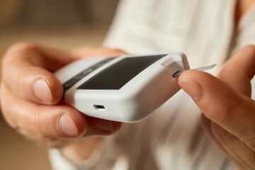 A person inserts a testing strip into a glucometer to check glucose levels. This activity occurs indoors, emphasizing the importance of monitoring diabetes regularly and maintaining health