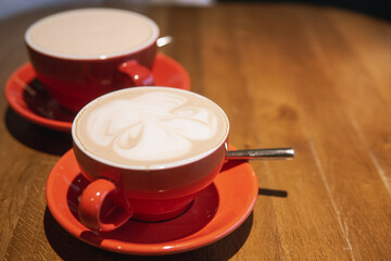 Artistic latte creations served in red cups on a wooden table. A perfect representation of a cozy cafe atmosphere for coffee lovers.