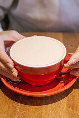 A cozy scene showing hands holding a red cup of a beverage on a wooden surface, highlighting a warm and inviting ambiance.