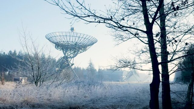 Large radio telescope standing in a field covered with frost on a cold winter morning