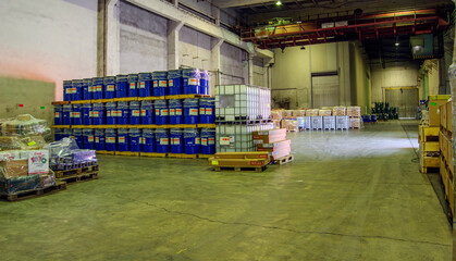 Blue barrels and other containers are neatly arranged on pallets in a spacious warehouse.Concrete floor and high ceiling give it an industrial feel,while the large open space allows for easy movement.