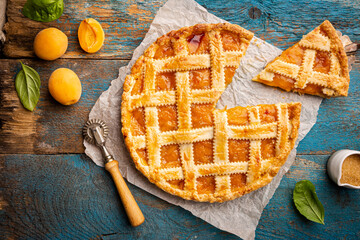 Summer apricot or peach pie homemade on blue wooden background, top view. Delicious fruit dessert....