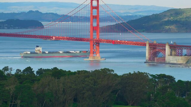 Aerial view of the magnificent Golden Gate Bridge with a cargo ship passing under it. This bridge connects the San Francisco peninsula to Marin County. US route 101 and SR 1 full of cars. Shot in 8K.