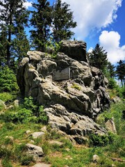 Rock formation with a historical plaque in Góry Sowie, Poland, surrounded by lush greenery and tall pines under a bright sky