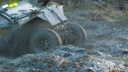 A close-up of a rugged, off-road vehicle splashing through a muddy course during a race. The...