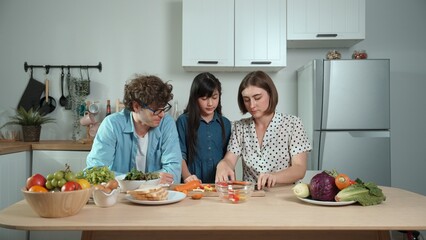 Happy father move to music while cooking food and prepare lunch at modern kitchen. Active dad dancing to song while making healthy food or salad surrounded with vegetable and kitchenware. Pedagogy.