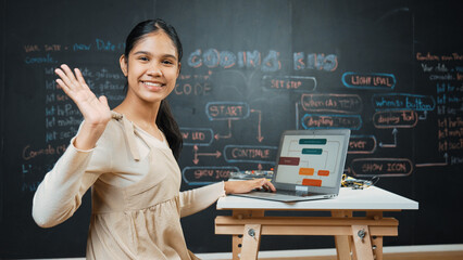 Smart highschool girl waving to camera while programing code at blackboard with engineering code or...