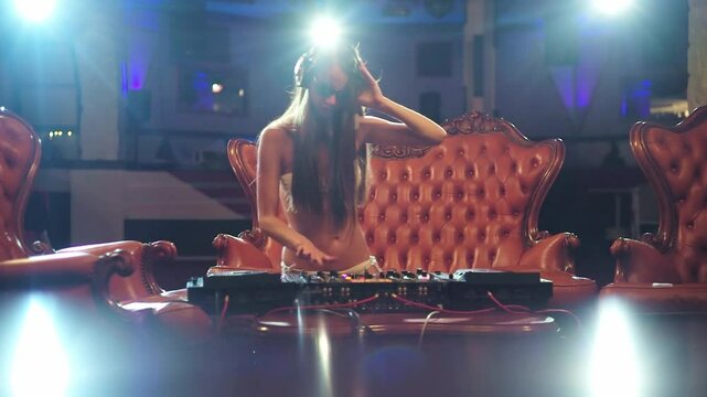 Sexy woman Dj mixing music at the club. Glamorous female DJ. Sexy Dj enjoying nightlife. Sexy clubbing girl with a headset. Sensual woman dancing to electronic music. Luxury nightclub scene with a DJ.