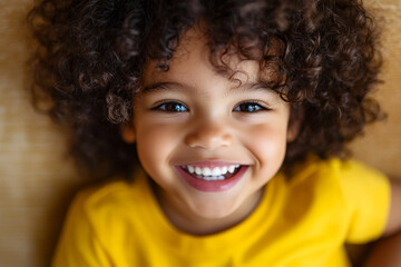 Close up portrait of a smiling young child with curly hair wearing a yellow shirt looking at the camera