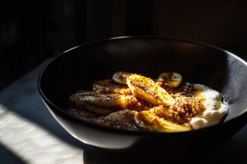 Fototapeta premium A quinoa bowl with caramelized banana and Greek yogurt, set against dramatic lighting, with harsh shadows creating a high-contrast atmosphere, perfect for a healthy breakfast