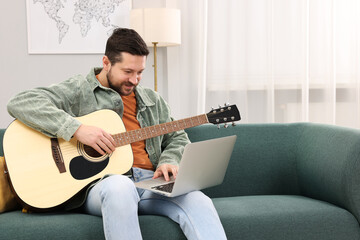 Relaxing hobby. Man playing guitar with online tutorial by laptop on sofa at home