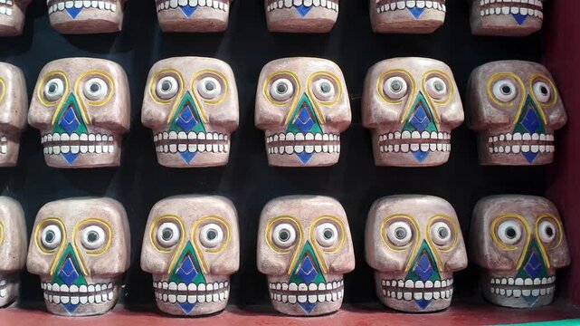A row of skulls with blue and green designs on them. They are all smiling. There are many skulls in the row