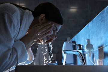 Woman washing her face over sink in bathroom
