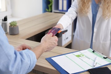 Receptionist taking payment from patient via terminal at counter in clinic, closeup