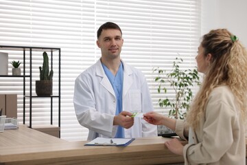Fototapeta premium Patient giving medical insurance card to smiling receptionist at counter in clinic