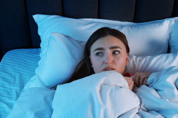 Fear of darkness. Scared young woman lying on bed in room at night