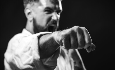 Karate man in kimono ready to fight. Sport and fitness. Strength and motivation. Angry karate master instructor practicing punches in gym at karate training. Selective focus on fist. Black and white.