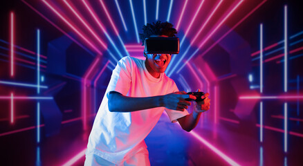 Teenager holding joystick and wearing VR goggles while enjoy playing games at neon abstract...