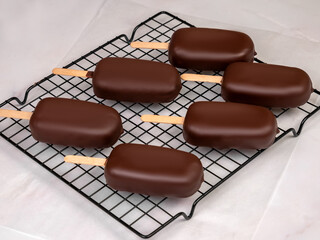 Chocolate-Covered Ice Cream Bar Stabilizing on Cooling Rack.  A freshly dipped chocolate-covered ice cream bar with a smooth, glossy surface rests on a cooling rack to stabilize. 