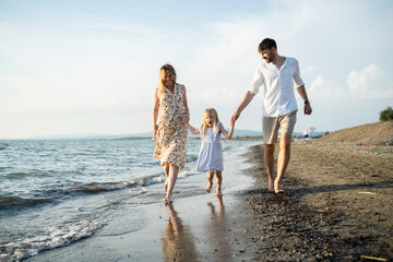 Happy family walking barefoot on a sandy beach at sunset