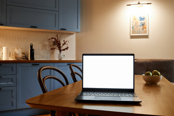 Laptop with blank screen sitting on wooden kitchen table surrounded by chairs in cozy kitchen environment featuring cabinets, counter, and wall decor