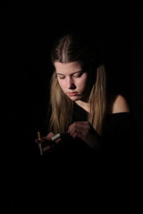 Obraz premium A young woman in the dark lights a cigarette, illuminated only by the flame of a lighter. Her face is focused, the background remains dark and blurred, creating an atmosphere of solitude, mystery