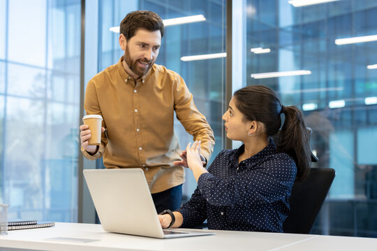 A woman holds up her hand to stop a man with a coffee cup in an office, potentially depicting workplace harassment.