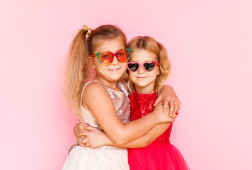 Two happy little girls hugging and laughing on a pink background